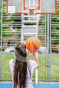 Young athletic woman is training to play basketball on modern outdoor basketball court. Happy woman