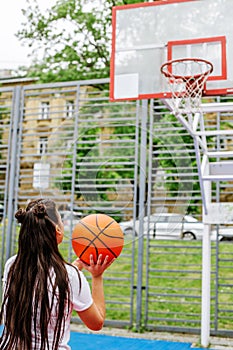 Young athletic woman is training to play basketball on modern outdoor basketball court. Vertical