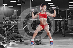 young athletics girl doing dumbbells press exercises sitting on bench in gym