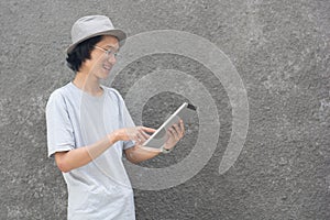 A young atractive creative asian man with fedora hat and glasses pointing at tablet computer and smiling