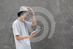 a young atractive creative asian man with fedora hat and glasses using tablet and smiling