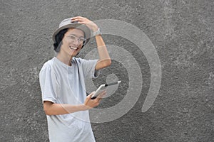 Young atractive creative asian man with fedora hat and glasses using tablet and smiling at camera