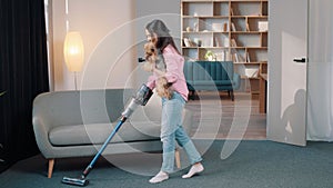 young atractive girl with a battery vacuum cleaner in the room holding little dog in her arms, cleaning