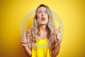 Young attactive woman wearing t-shirt standing over yellow  background amazed and surprised looking up and pointing with