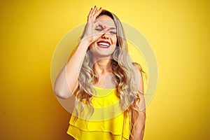 Young attactive woman wearing t-shirt standing over yellow  background doing ok gesture with hand smiling, eye looking