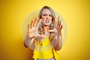 Young attactive woman wearing t-shirt standing over yellow isolated background afraid and terrified with fear expression stop