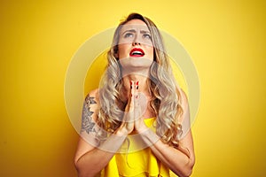 Young attactive woman wearing t-shirt standing over yellow isolated background begging and praying with hands together with hope