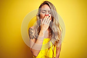 Young attactive woman wearing t-shirt standing over yellow isolated background bored yawning tired covering mouth with hand