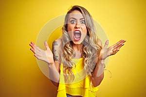 Young attactive woman wearing t-shirt standing over yellow isolated background celebrating crazy and amazed for success with arms