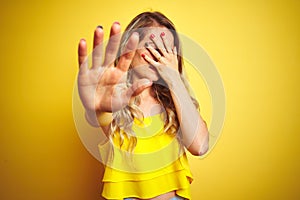 Young attactive woman wearing t-shirt standing over yellow isolated background covering eyes with hands and doing stop gesture