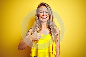 Young attactive woman wearing t-shirt standing over yellow isolated background doing happy thumbs up gesture with hand