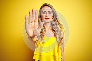 Young attactive woman wearing t-shirt standing over yellow isolated background doing stop sing with palm of the hand