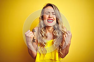 Young attactive woman wearing t-shirt standing over yellow isolated background excited for success with arms raised and eyes