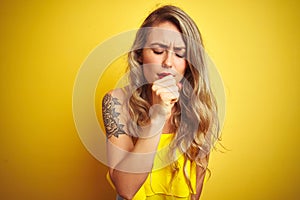 Young attactive woman wearing t-shirt standing over yellow isolated background feeling unwell and coughing as symptom for cold or