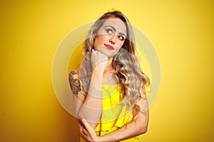 Young attactive woman wearing t-shirt standing over yellow isolated background with hand on chin thinking about question, pensive