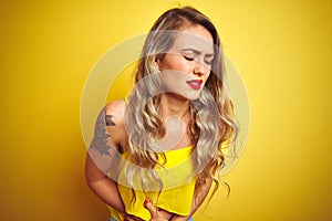 Young attactive woman wearing t-shirt standing over yellow isolated background with hand on stomach because indigestion, painful