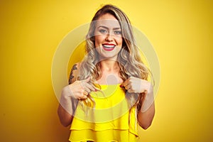 Young attactive woman wearing t-shirt standing over yellow isolated background looking confident with smile on face, pointing