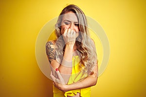 Young attactive woman wearing t-shirt standing over yellow isolated background looking stressed and nervous with hands on mouth