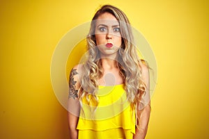 Young attactive woman wearing t-shirt standing over yellow isolated background puffing cheeks with funny face