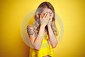 Young attactive woman wearing t-shirt standing over yellow isolated background with sad expression covering face with hands while