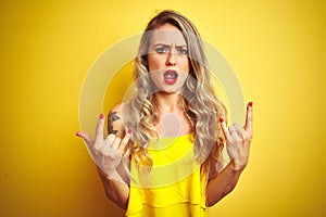 Young attactive woman wearing t-shirt standing over yellow isolated background shouting with crazy expression doing rock symbol