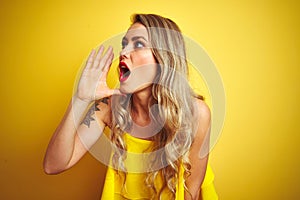 Young attactive woman wearing t-shirt standing over yellow isolated background shouting and screaming loud to side with hand on