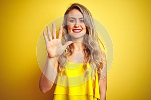 Young attactive woman wearing t-shirt standing over yellow isolated background showing and pointing up with fingers number five