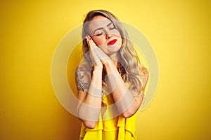 Young attactive woman wearing t-shirt standing over yellow isolated background sleeping tired dreaming and posing with hands