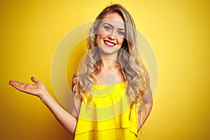 Young attactive woman wearing t-shirt standing over yellow isolated background smiling cheerful presenting and pointing with palm