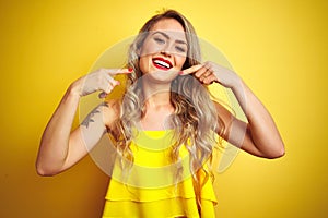 Young attactive woman wearing t-shirt standing over yellow isolated background smiling cheerful showing and pointing with fingers