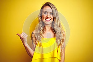 Young attactive woman wearing t-shirt standing over yellow isolated background smiling with happy face looking and pointing to the