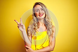 Young attactive woman wearing t-shirt standing over yellow isolated background smiling with happy face winking at the camera doing