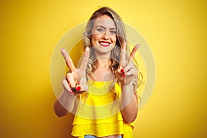 Young attactive woman wearing t-shirt standing over yellow isolated background smiling looking to the camera showing fingers doing