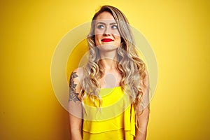 Young attactive woman wearing t-shirt standing over yellow isolated background smiling looking to the side and staring away