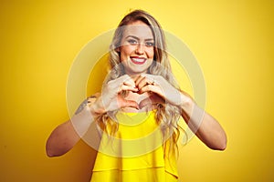 Young attactive woman wearing t-shirt standing over yellow isolated background smiling in love doing heart symbol shape with hands