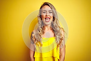 Young attactive woman wearing t-shirt standing over yellow isolated background sticking tongue out happy with funny expression