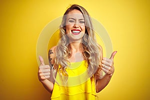 Young attactive woman wearing t-shirt standing over yellow isolated background success sign doing positive gesture with hand,
