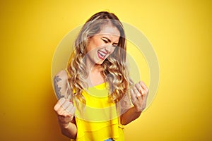 Young attactive woman wearing t-shirt standing over yellow isolated background very happy and excited doing winner gesture with