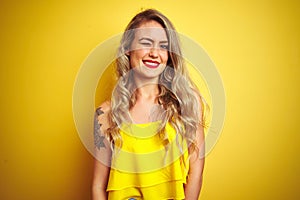 Young attactive woman wearing t-shirt standing over yellow isolated background winking looking at the camera with sexy expression,