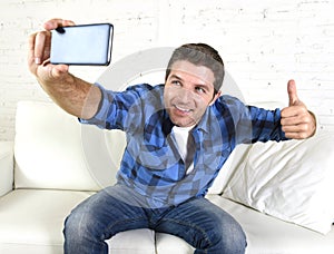 Young attractive 30s man taking selfie picture or self video with mobile phone at home sitting on couch smiling happy