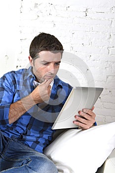 Young attractive 30s man using digital tablet pad lying on couch at home networking looking relaxed