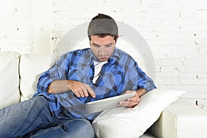 Young attractive 30s man using digital tablet pad lying on couch at home networking looking relaxed