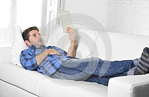 Young attractive 30s man using digital tablet pad lying on couch at home networking looking relaxed