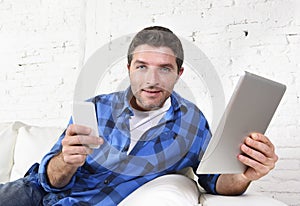 Young attractive 30s man using mobile phone and digital tablet pad on couch smiling happy