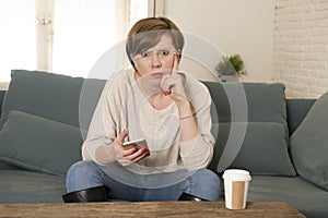 Young attractive 30s red hair woman upset bored and moody using internet app on mobile phone sitting at home sofa couch in annoyed