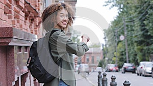 Young attractive african american girl with curly hair standing back, looking over shoulder making hand gesture inviting