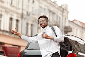 Young attractive African man hailing cab taxi on city street, raises his hand