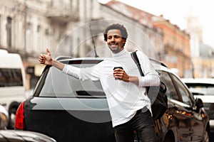 Young attractive African man hailing cab taxi on city street, raises his hand