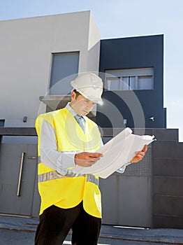 Young attractive architect worker supervising building blueprints outdoors wearing construction helmet