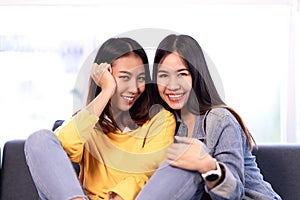 Young attractive asian girlfriends sitting together at couch sofa at home smiling and looking at camera